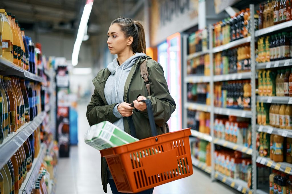 Young woman looking at products of shelves while buying in supermarket.